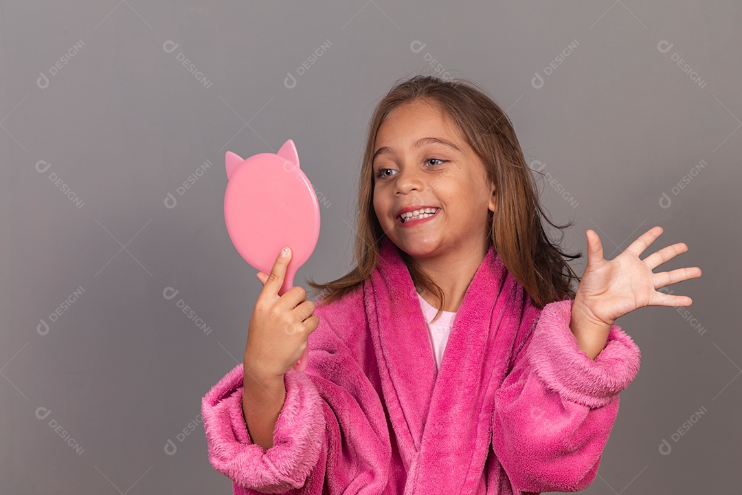 Linda menina usando roupão de banho rosa sobre fundo isolado segurando espelho