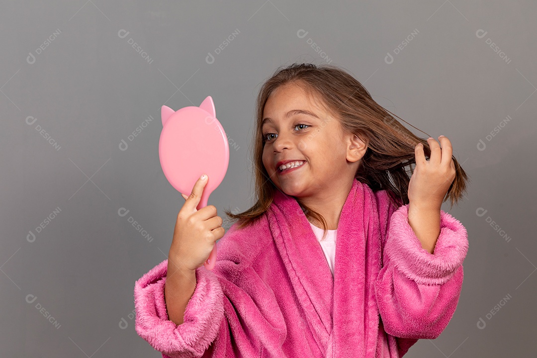 Linda menina usando roupão de banho rosa sobre fundo isolado segurando espelho