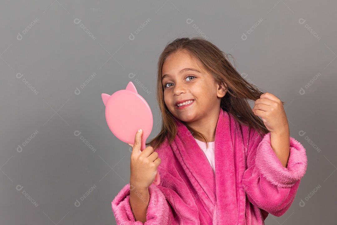 Linda menina usando roupão de banho rosa sobre fundo isolado segurando espelho