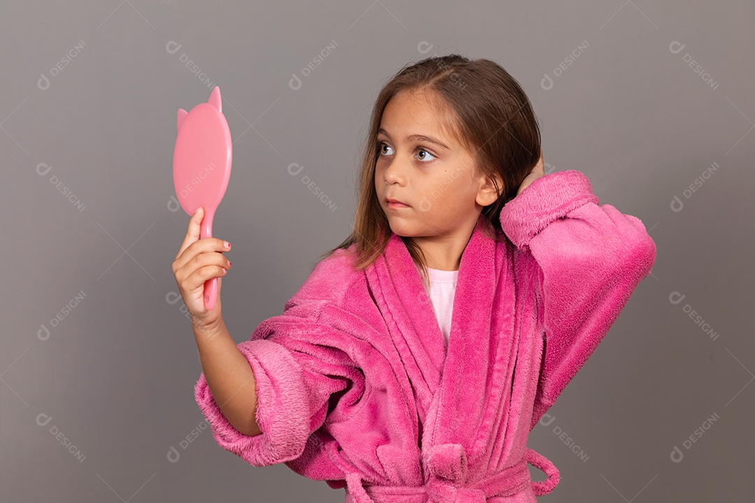 Linda menina usando roupão de banho rosa sobre fundo isolado segurando espelho