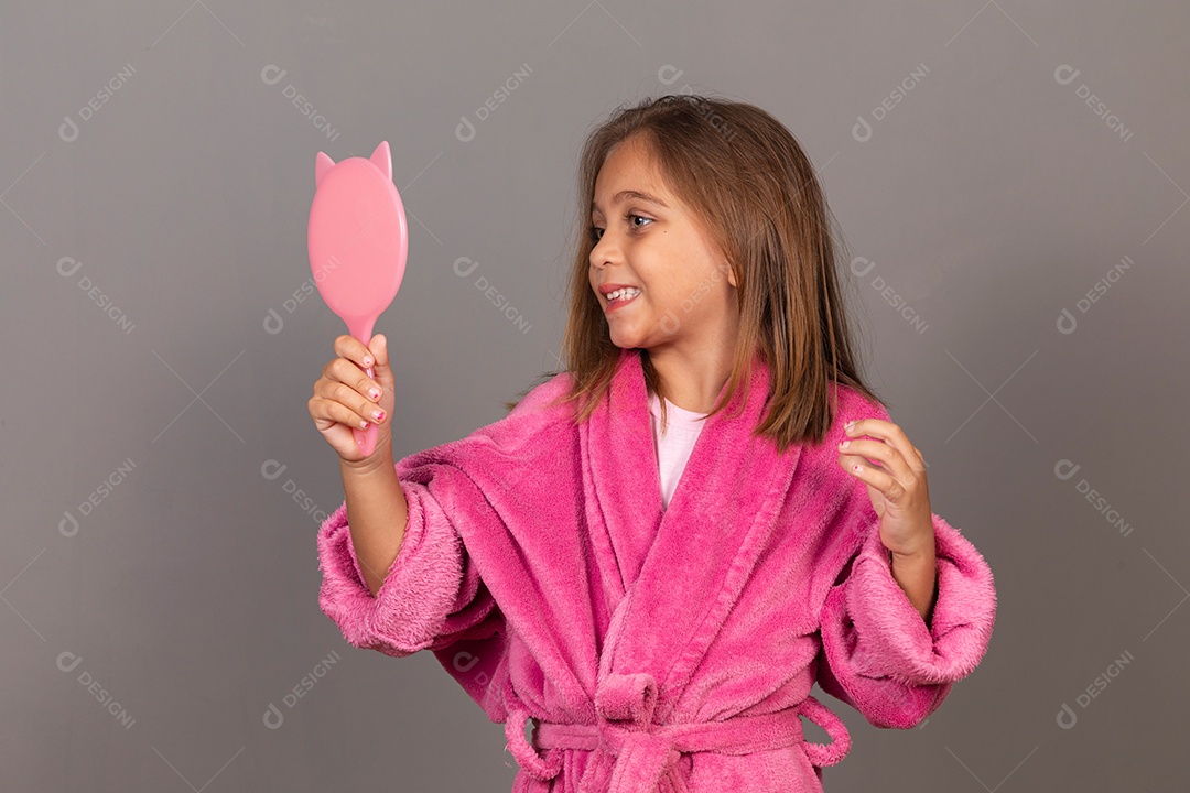 Linda menina usando roupão de banho rosa sobre fundo isolado segurando espelho
