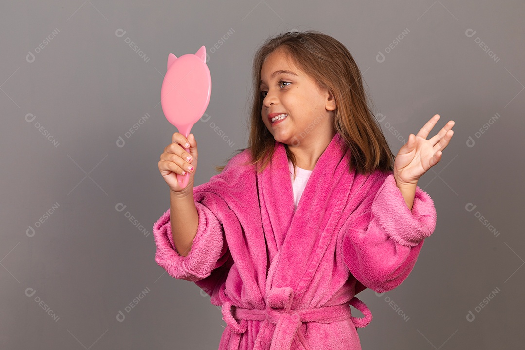 Linda menina usando roupão de banho rosa sobre fundo isolado segurando espelho