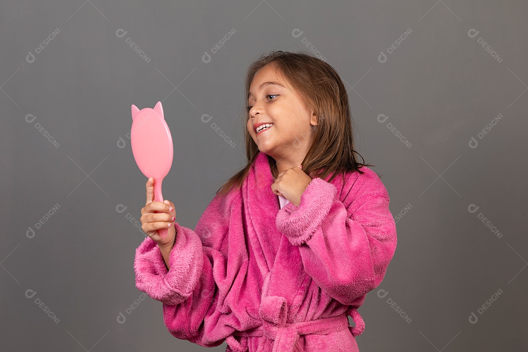 Linda menina usando roupão de banho rosa sobre fundo isolado segurando espelho