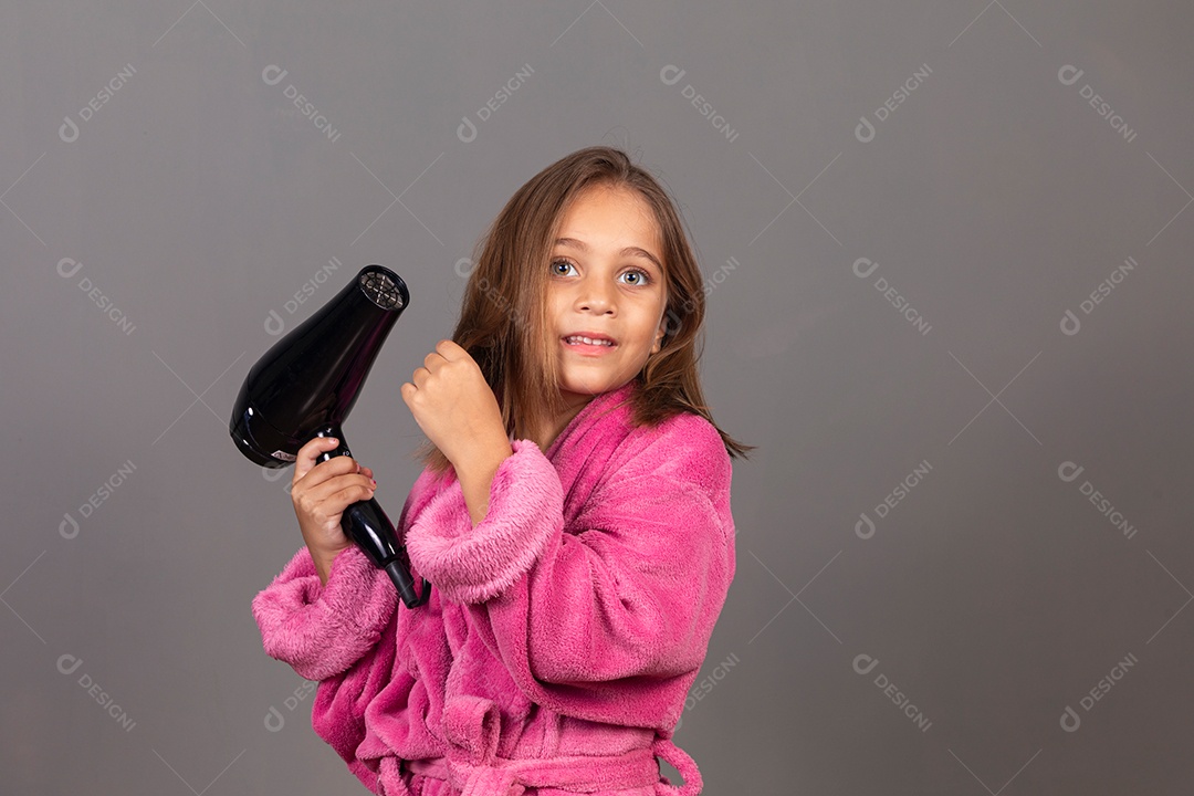 Linda menina usando roupão de banho rosa sobre fundo isolado segurando secador de cabelo
