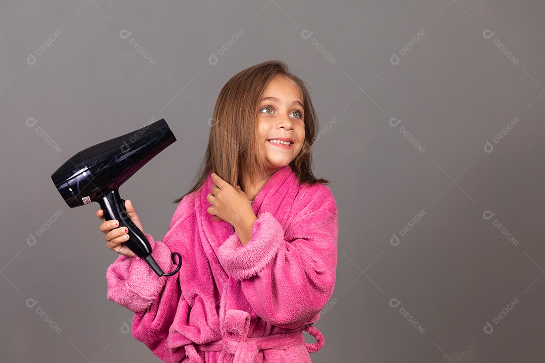 Linda menina usando roupão de banho rosa sobre fundo isolado segurando secador de cabelo