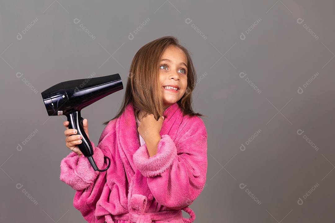 Linda menina usando roupão de banho rosa sobre fundo isolado segurando secador de cabelo