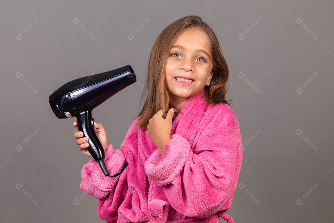 Linda menina usando roupão de banho rosa sobre fundo isolado segurando secador de cabelo