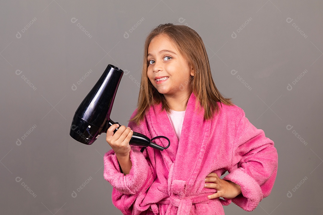 Linda menina usando roupão de banho rosa sobre fundo isolado segurando secador de cabelo
