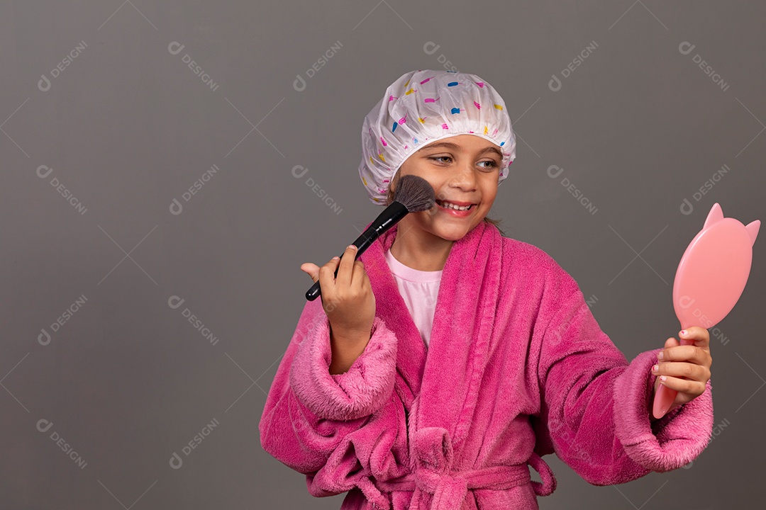 Linda menina usando roupão de banho rosa touca pincel e espelho sobre fundo isolado