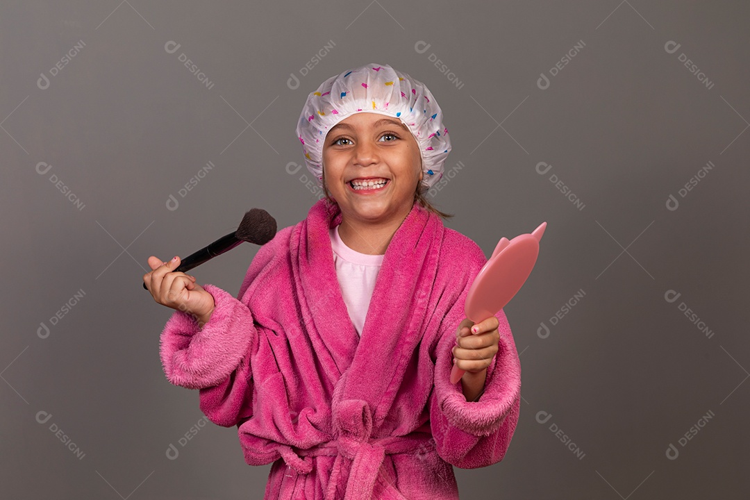 Linda menina usando roupão de banho rosa touca pincel e espelho sobre fundo isolado