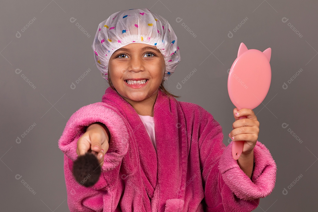 Linda menina usando roupão de banho rosa segurando espelho touca sobre fundo isolado