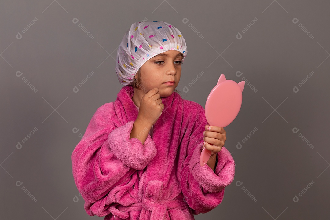 Linda menina usando roupão de banho rosa segurando espelho touca sobre fundo isolado