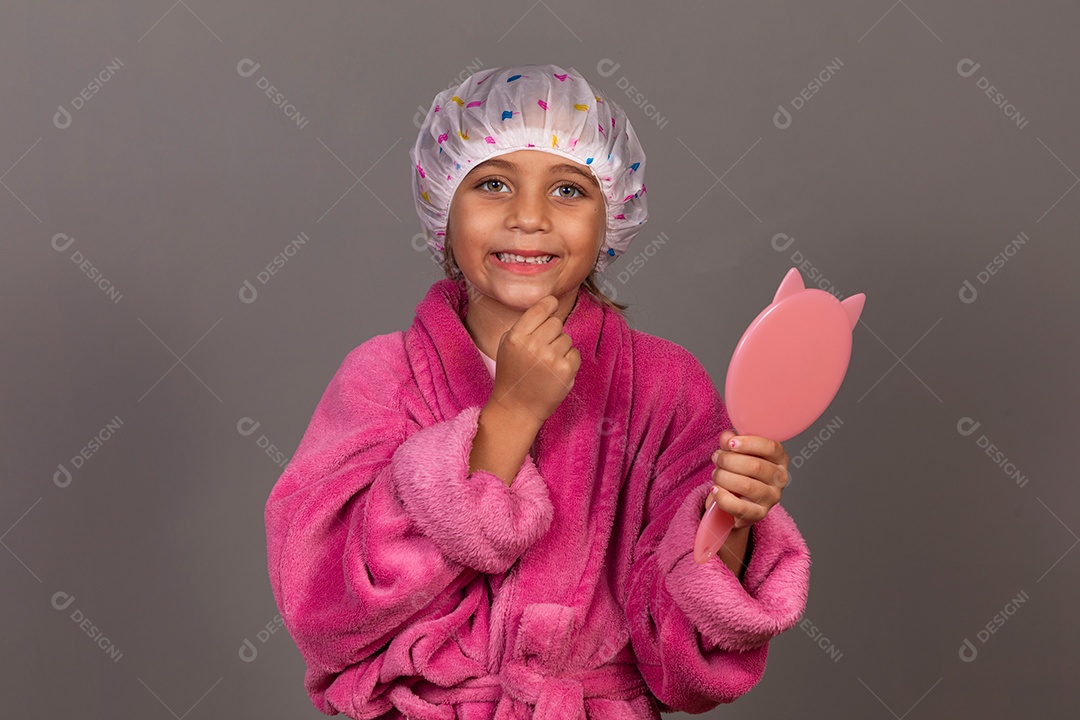 Linda menina usando roupão de banho rosa segurando espelho touca sobre fundo isolado