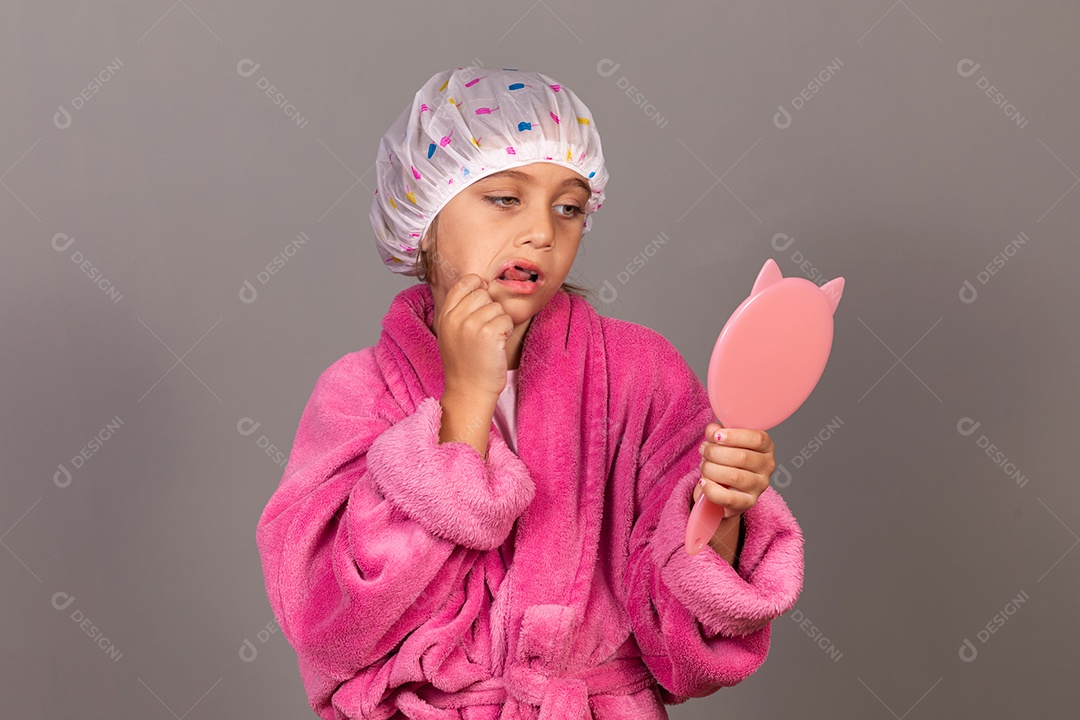 Linda menina usando roupão de banho rosa segurando espelho touca sobre fundo isolado