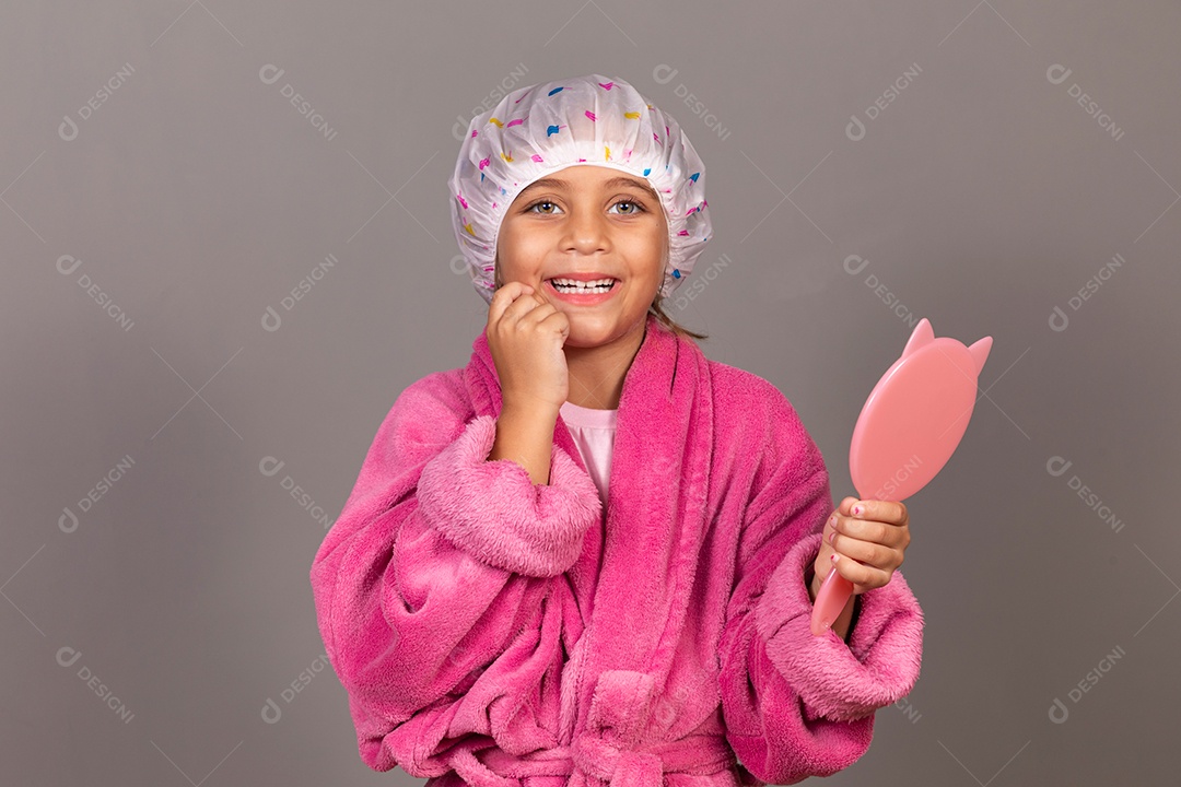 Linda menina usando roupão de banho rosa segurando espelho touca sobre fundo isolado