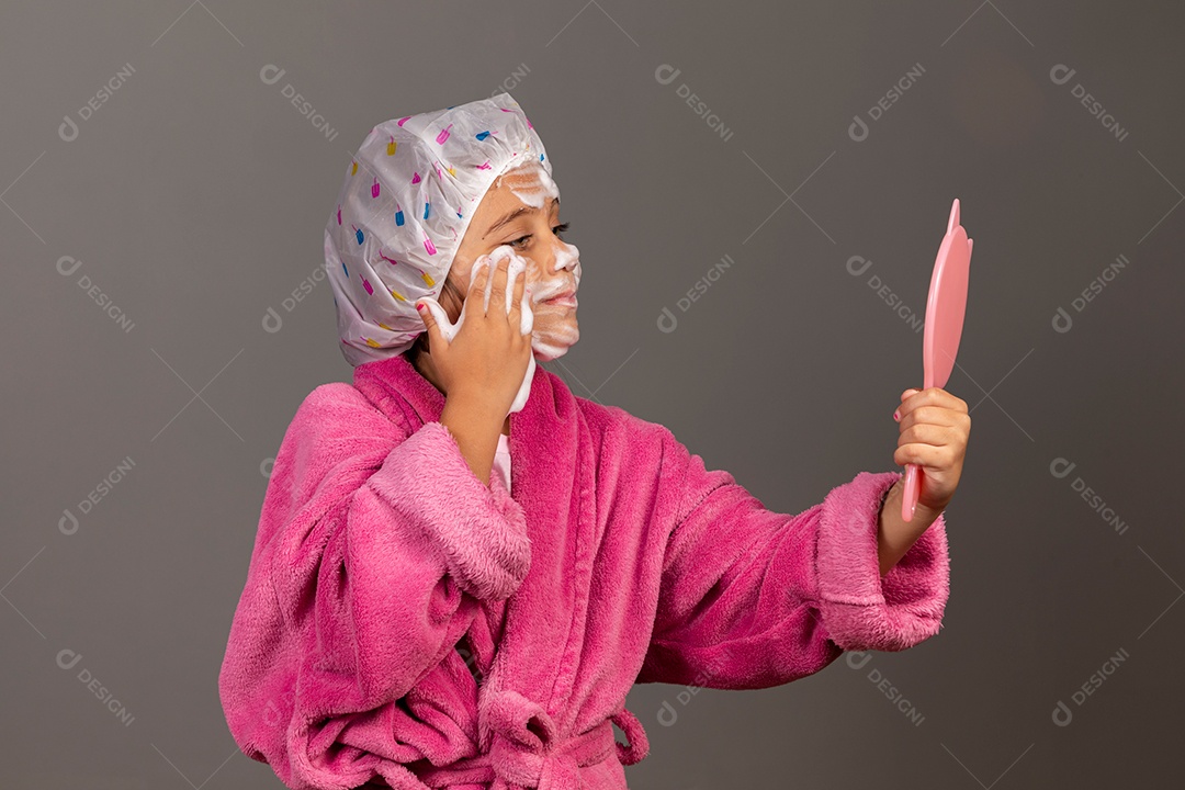 Linda menina usando roupão de banho rosa touca esfoliante e espelho sobre fundo isolado