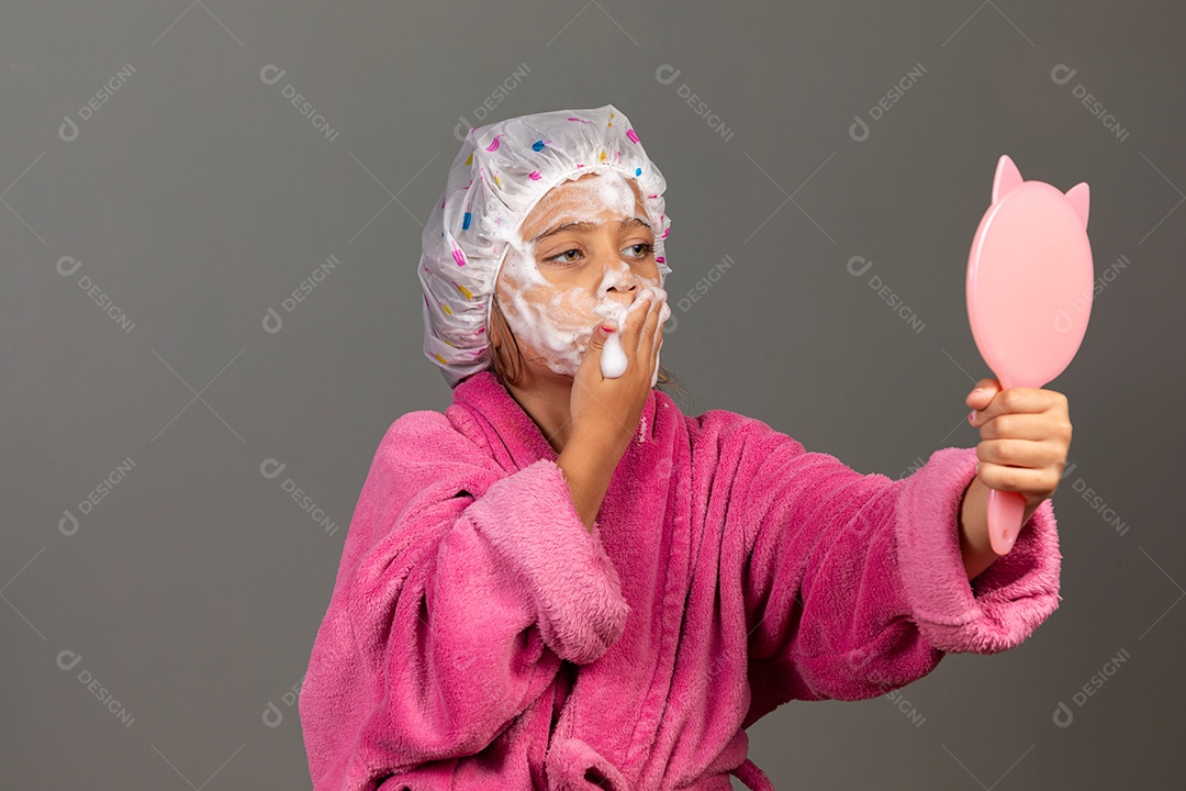 Linda menina usando roupão de banho rosa touca esfoliante e espelho sobre fundo isolado