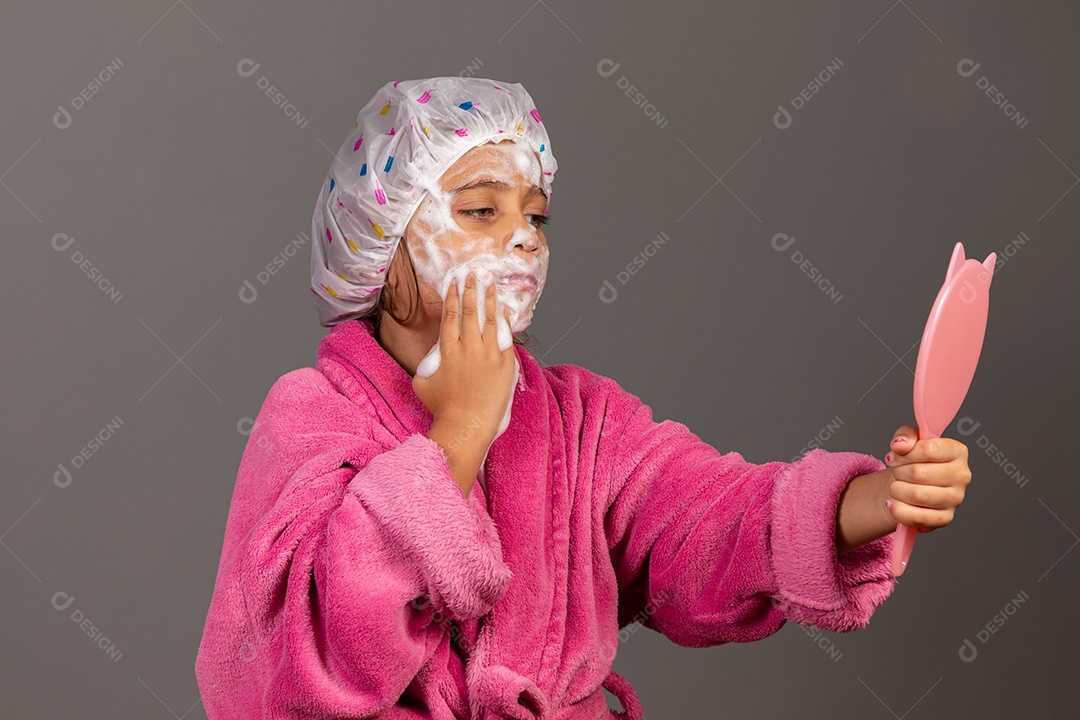 Linda menina usando roupão de banho rosa touca esfoliante e espelho sobre fundo isolado