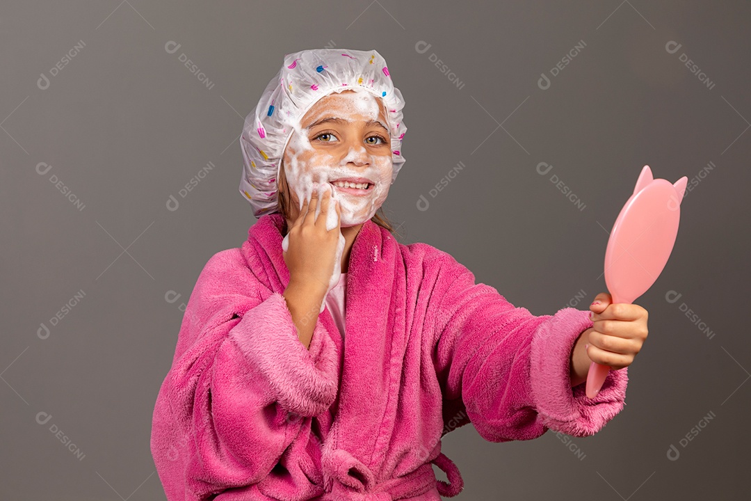 Linda menina usando roupão de banho rosa touca esfoliante e espelho sobre fundo isolado