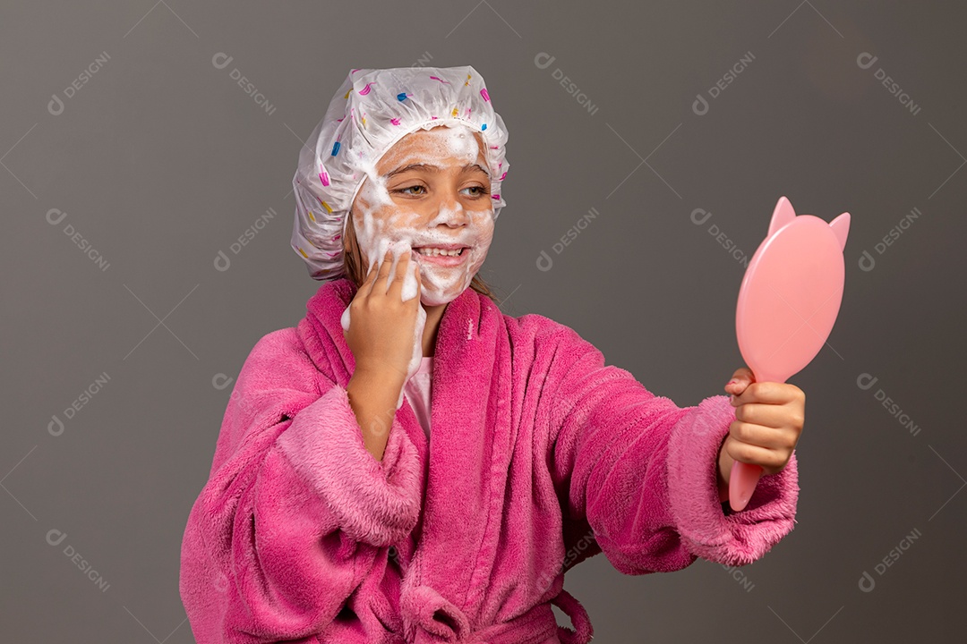 Linda menina usando roupão de banho rosa touca esfoliante e espelho sobre fundo isolado