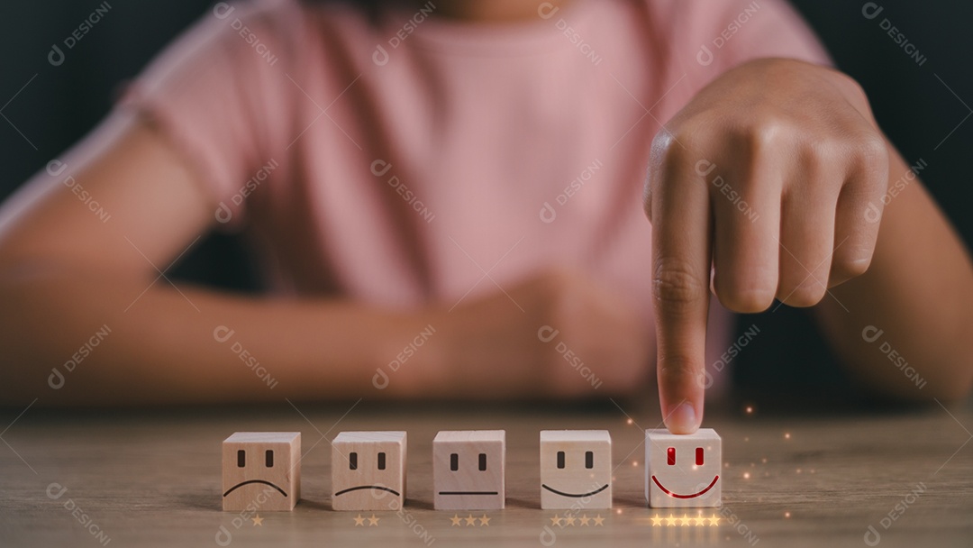 Mão de pessoa tocando em bloco de madeira com caras de avaliações sobre mesa de madeira