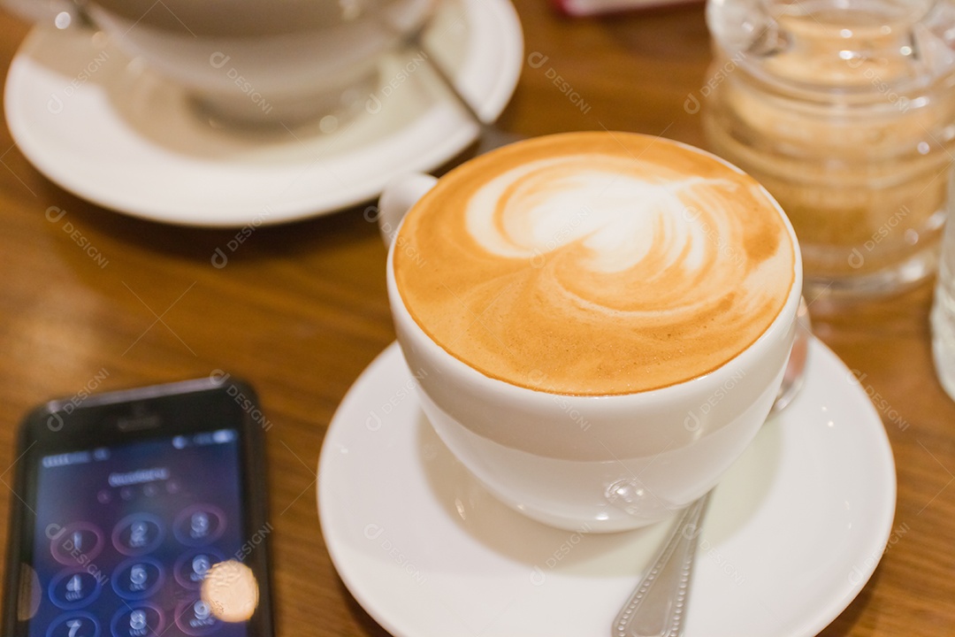 Cappuccino em xícara em prato ao lado de smartphone tecnologia avançada sobre mesa de madeira