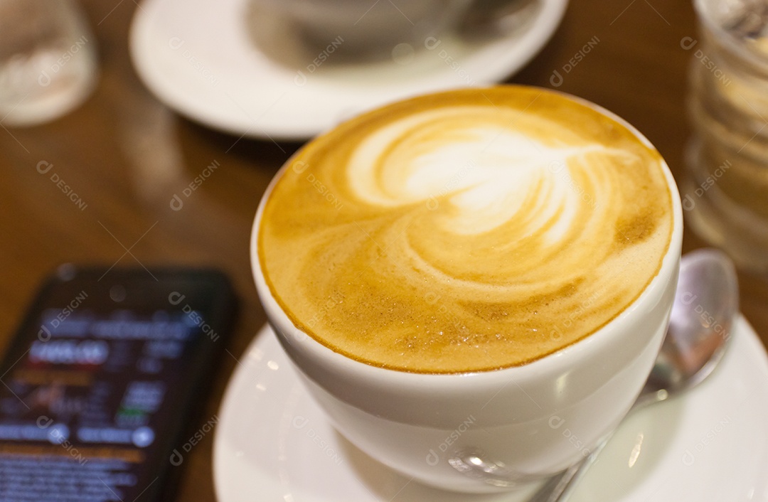 Cappuccino em xícara em prato ao lado de smartphone tecnologia avançada sobre mesa de madeira
