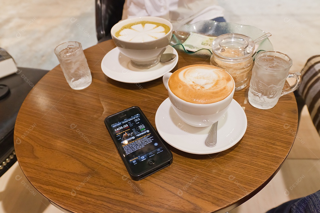 Nota de banco tailandesa em tijela ao lado de smrtphone com tecnologia avançada para investimento e xícara de cappuccino sobre mesa de madeira