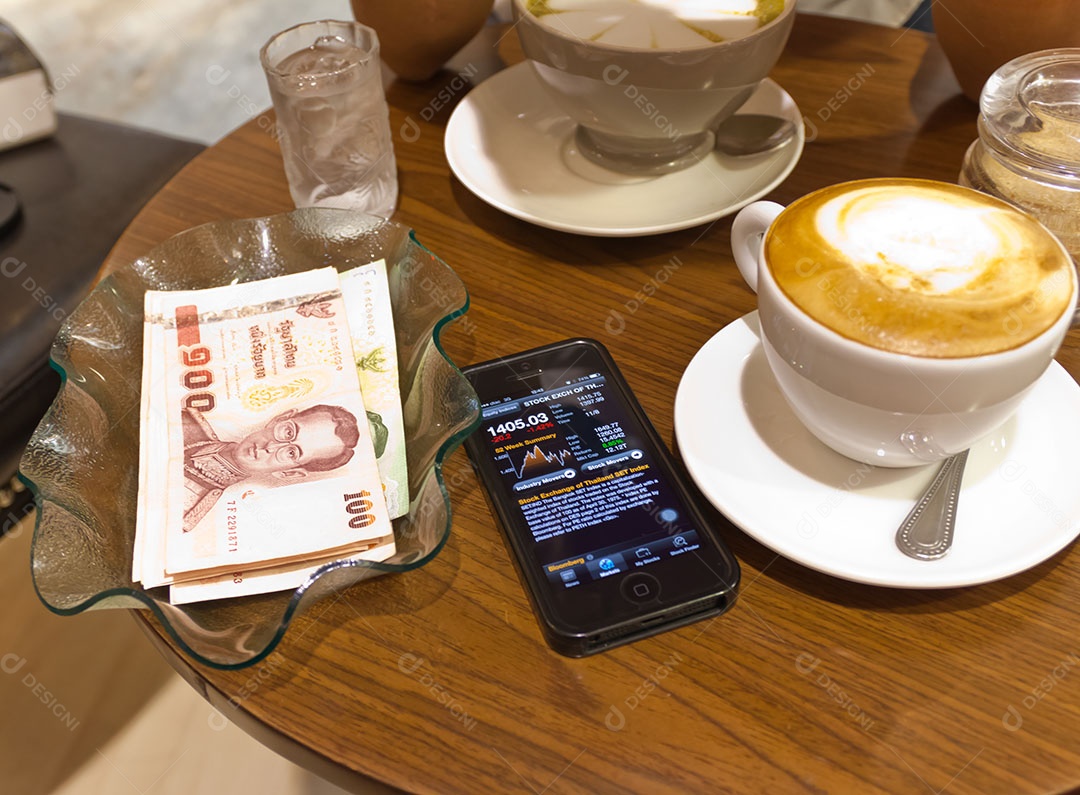 Nota de banco tailandesa em tijela ao lado de smrtphone com tecnologia avançada para investimento e uma xícara de cappuccino sobre mesa de madeira