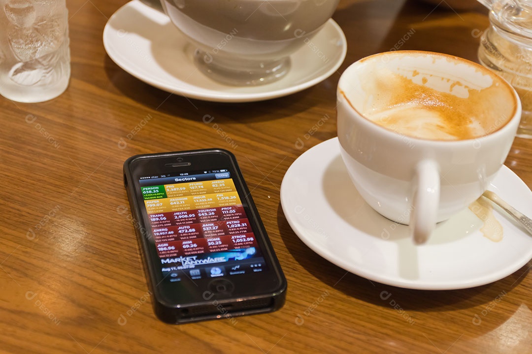 Smartphone ao lado de xícara de café sobre uma mesa de madeira