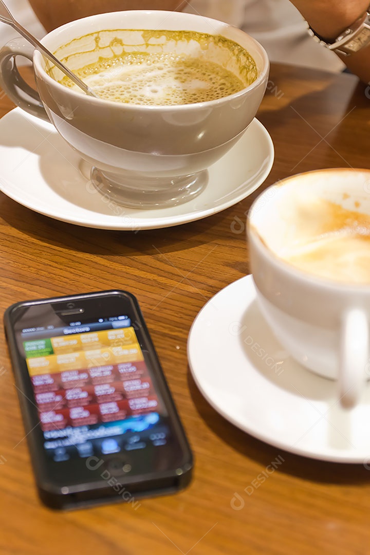 Smartphone ao lado de xícara de café sobre uma mesa de madeira
