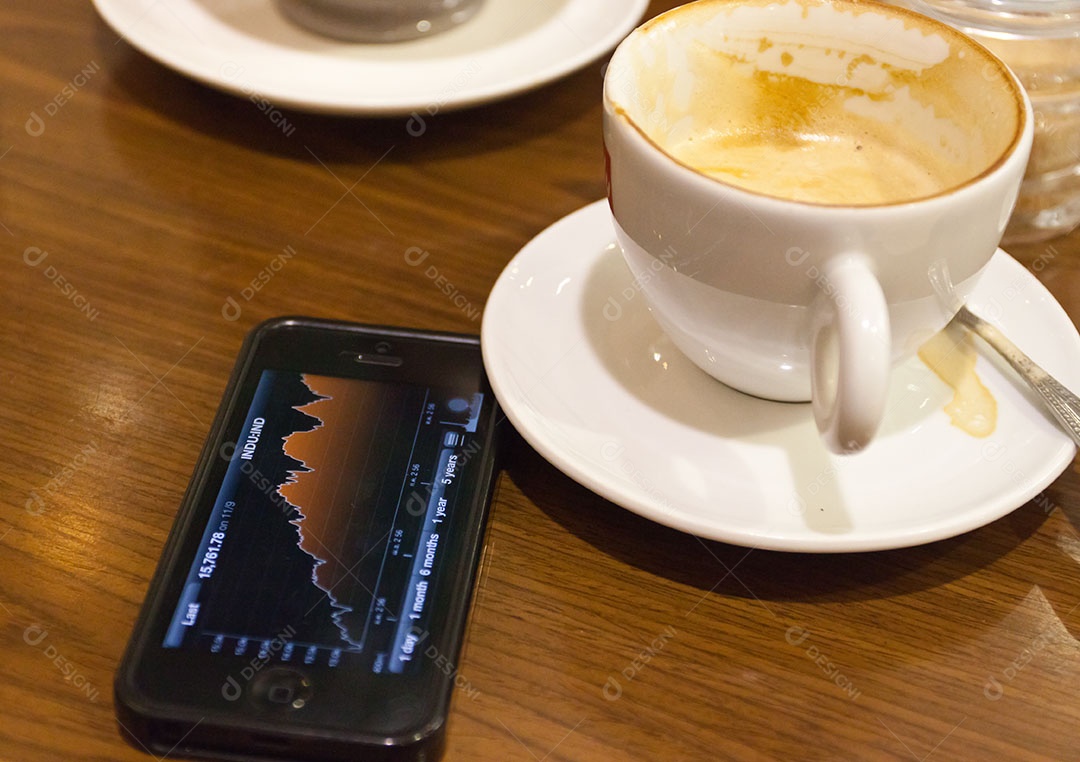 Smartphone ao lado de xícara de café sobre uma mesa de madeira
