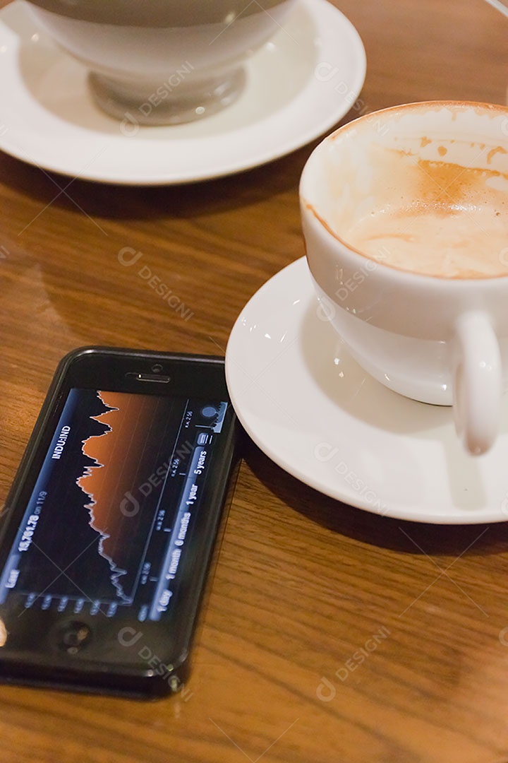Smartphone ao lado de xícara de café sobre uma mesa de madeira