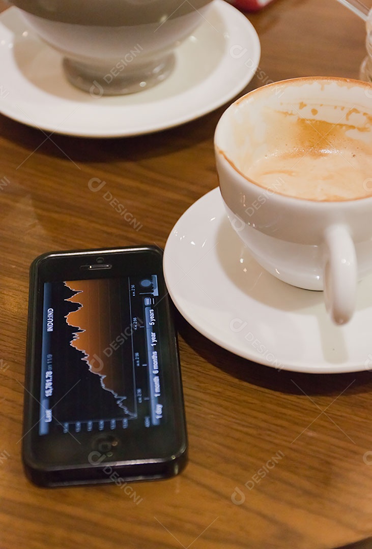 Smartphone ao lado de xícara de café sobre uma mesa de madeira