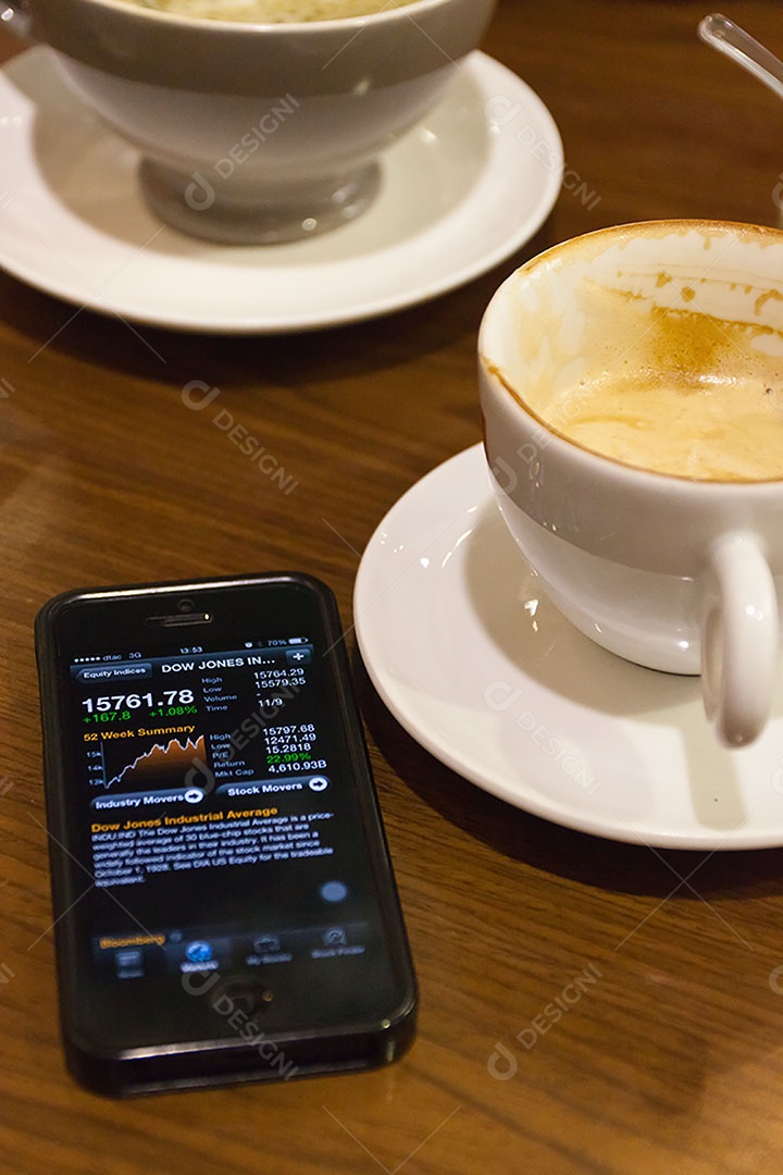 Smartphone ao lado de xícara de café sobre uma mesa de madeira