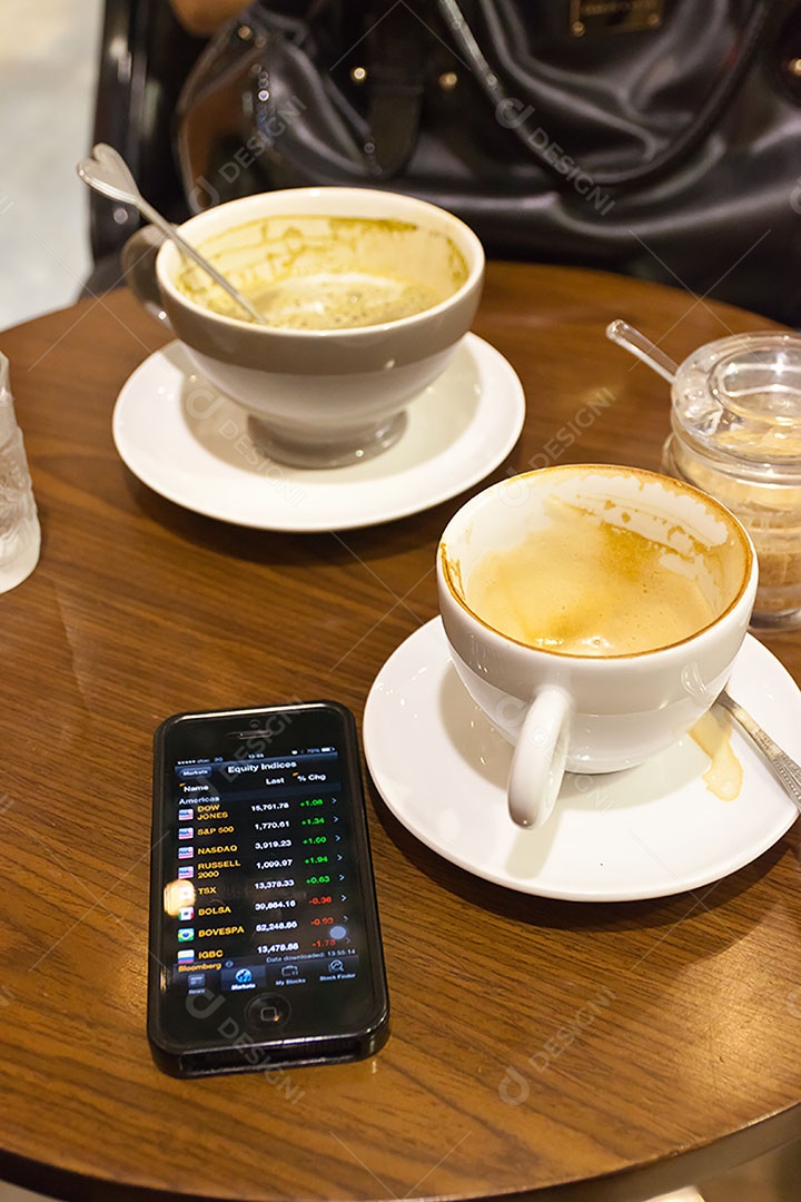 Smartphone ao lado de xícara de café sobre uma mesa de madeira