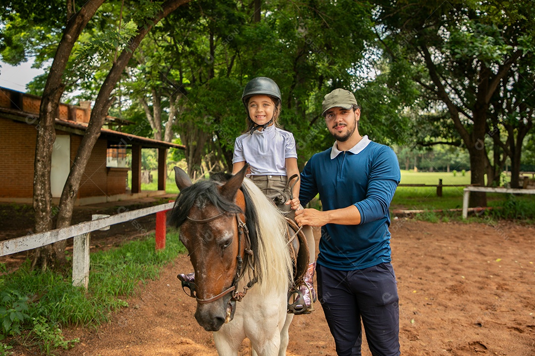 Filha montada a cavalo ao lado do seu pai sobre uma fazenda
