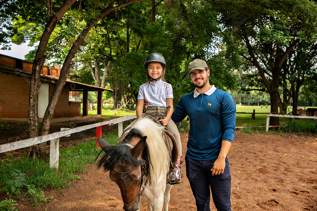 Filha montada a cavalo ao lado do seu pai sobre uma fazenda