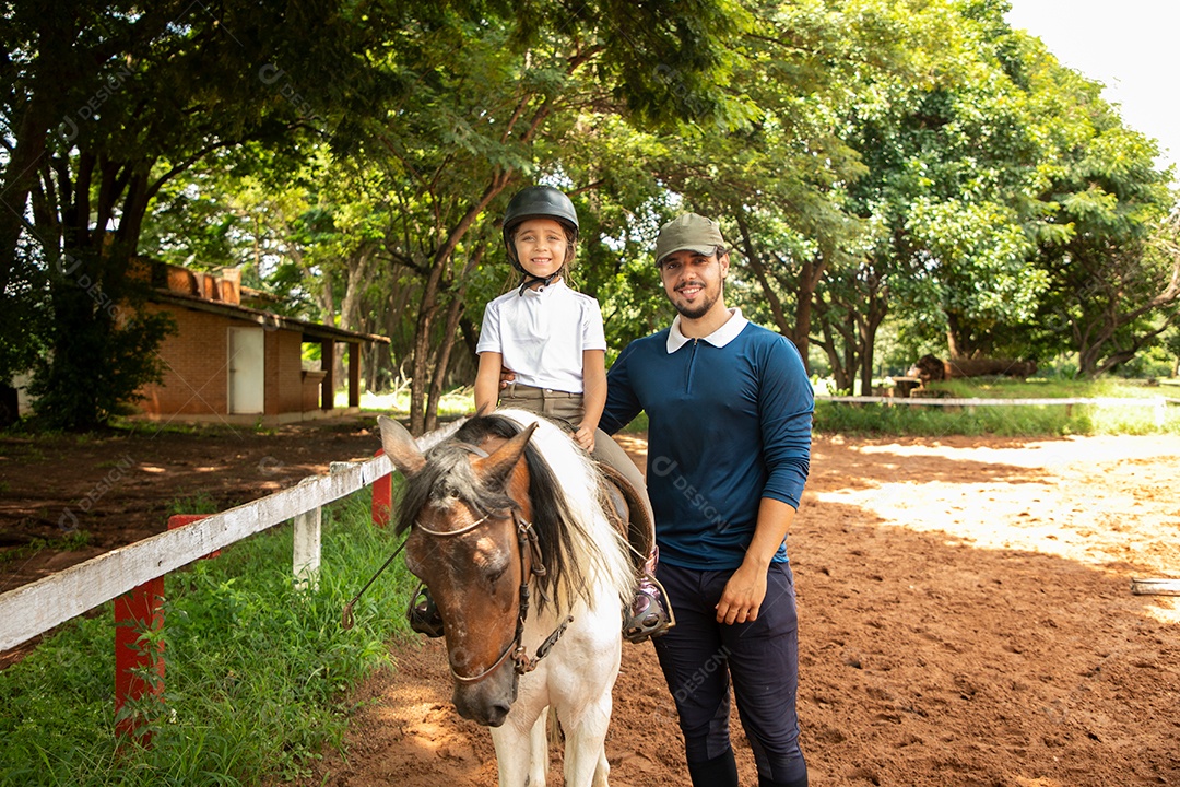 Filha montada a cavalo ao lado do seu pai sobre uma fazenda