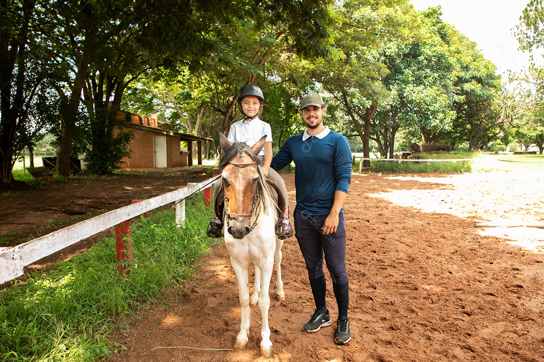 Filha montada a cavalo ao lado do seu pai sobre uma fazenda