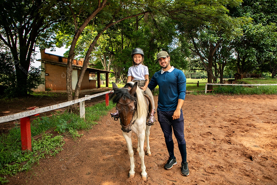 Filha montada a cavalo ao lado do seu pai sobre uma fazenda