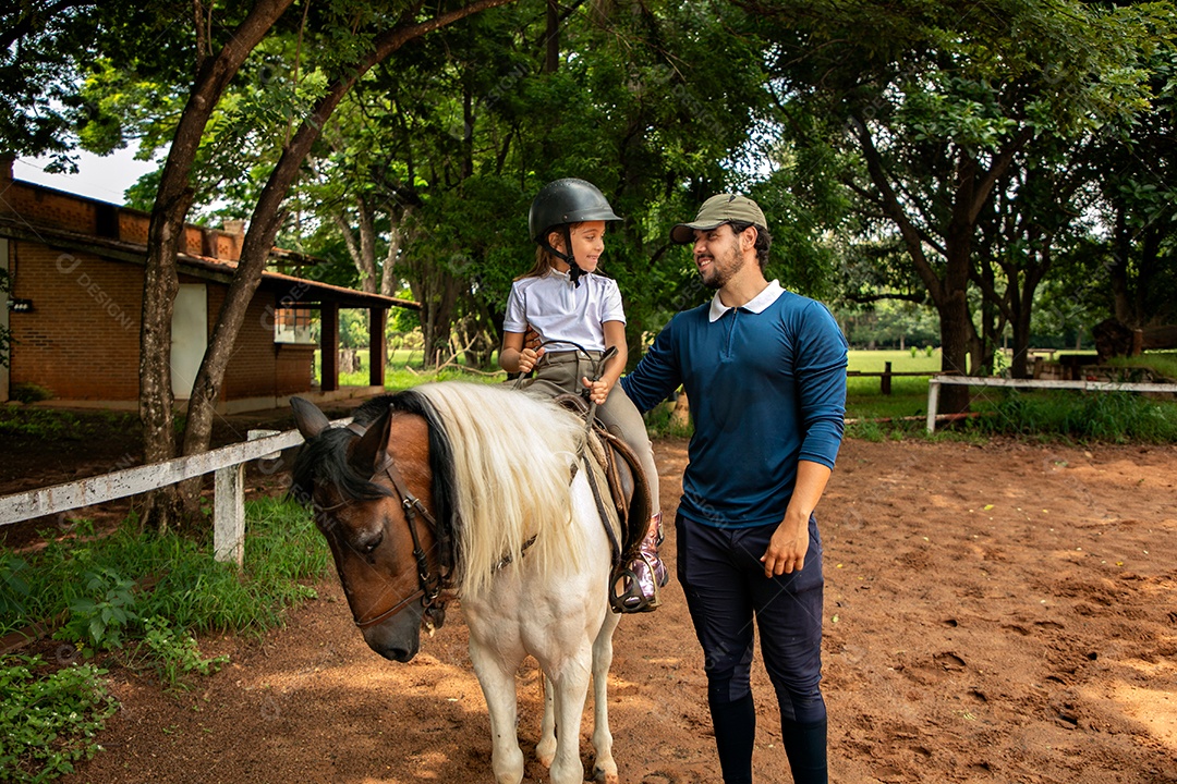 Filha montada a cavalo ao lado do seu pai sobre uma fazenda