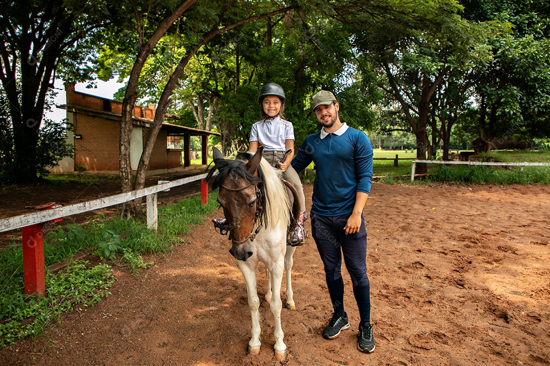 Filha montada a cavalo ao lado do seu pai sobre uma fazenda