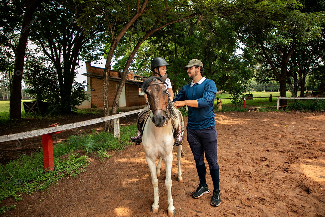 Filha montada a cavalo ao lado do seu pai sobre uma fazenda