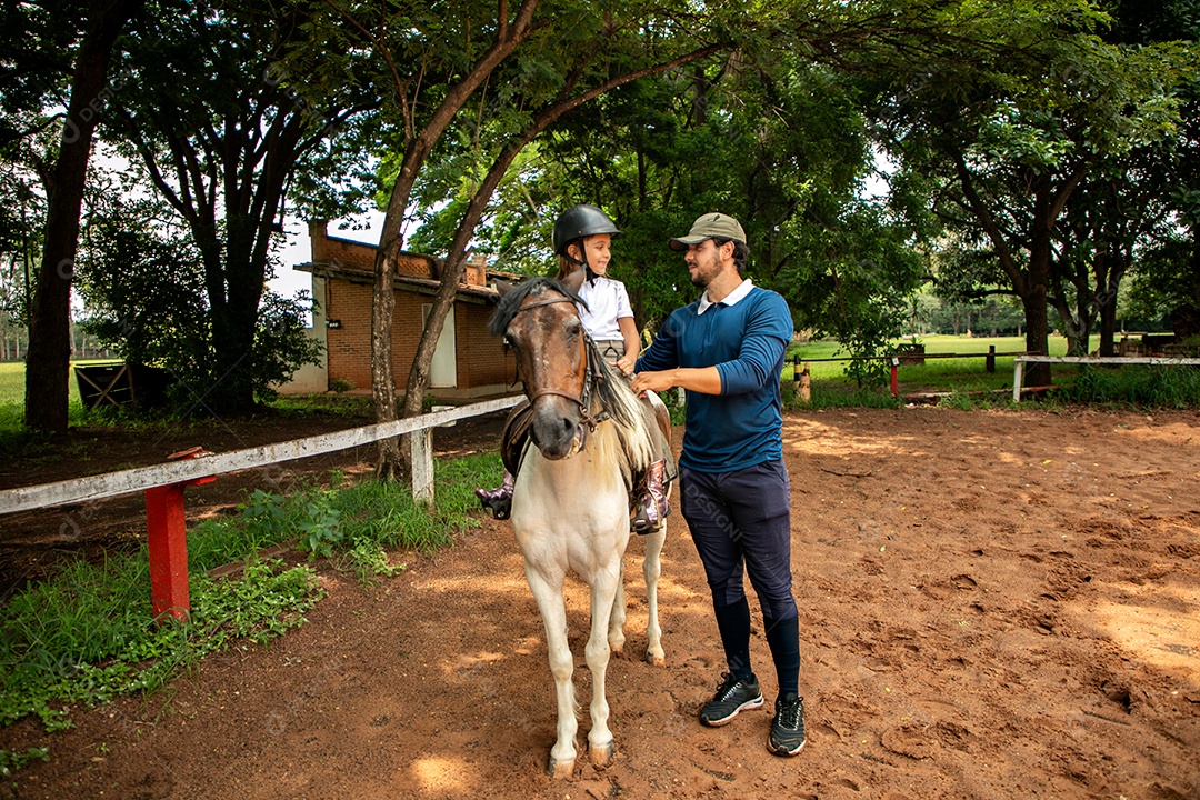 Filha montada a cavalo ao lado do seu pai sobre uma fazenda