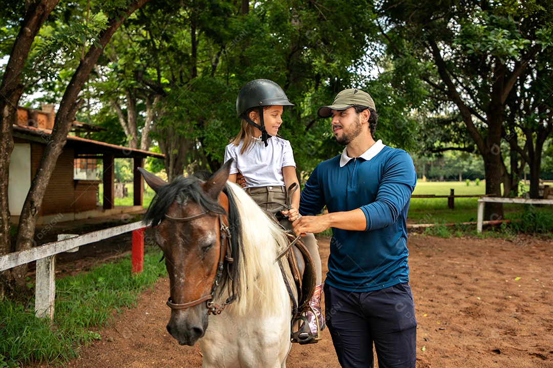 Filha montada a cavalo ao lado do seu pai sobre uma fazenda