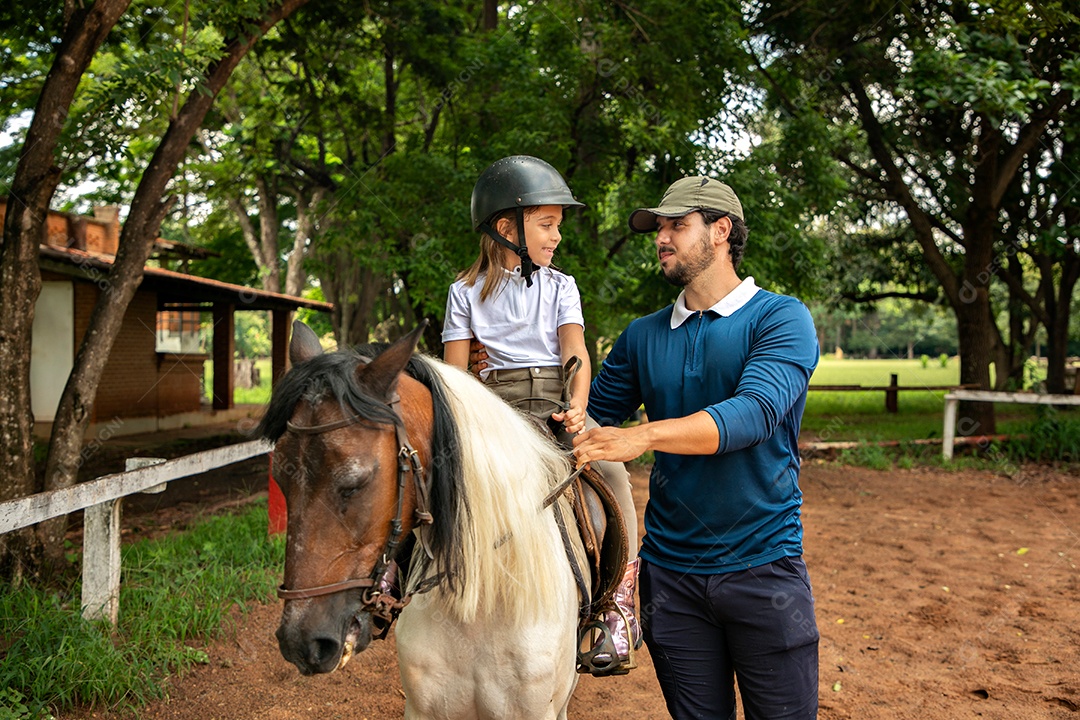 Filha montada a cavalo ao lado do seu pai sobre uma fazenda