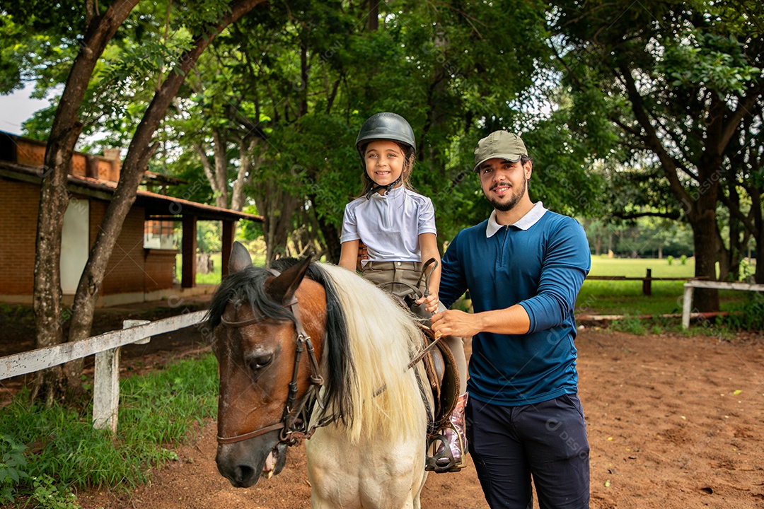 Filha montada a cavalo ao lado do seu pai sobre uma fazenda
