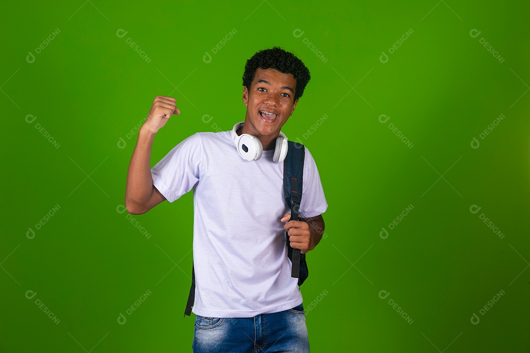 Lindo garoto negro usando fone de ouvido e mochila sobre fundo verde isolado