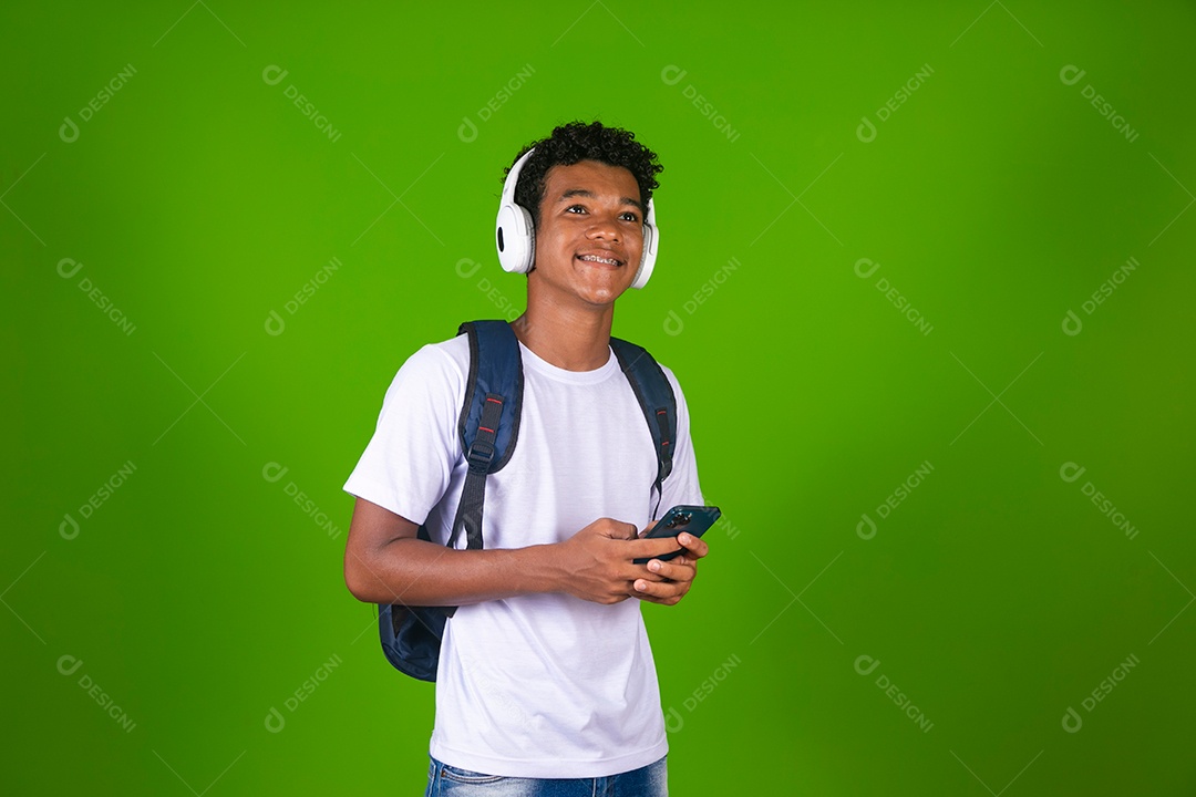 Lindo garoto negro usando fone de ouvido e mochila e segurando smartfhone sobre fundo verde isolado